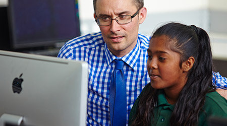 A boy sitting and smiling while using his computer at school