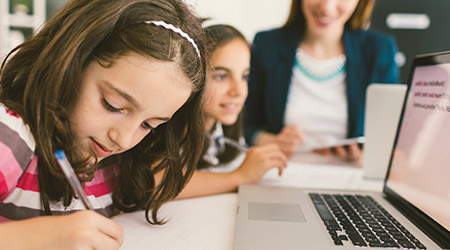 A female teacher sitting inbetween two students, helping them to read.