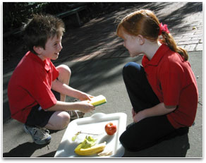 Two young students are in conversation over a tray of fruit.