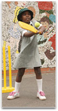 A young girl attempting to hit a ball with a yellow plastic cricket bat