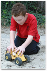 A young student in a sand pit pushing a model grader along to form a road.