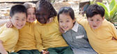 A group of young school children sitting outside with their arms around each other
