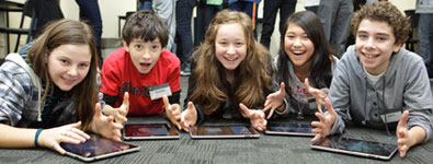 Five students lying on the floor with their iPads and smiling