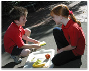 Two young students are in conversation over a tray of fruit.