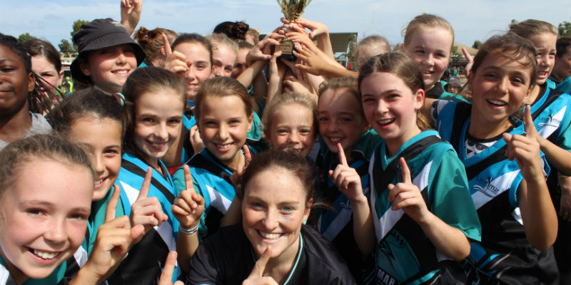  group of girls in sports gear hold a trophy aloft