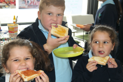 three primary school childre, one boy two girls,children eating toast for breakfast