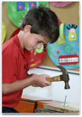 A young student is hammering a large nail into a beam of wood.
