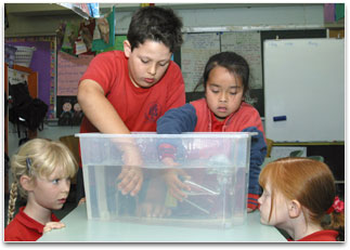 2 students are holding glasses under the water which are containing trapped air.